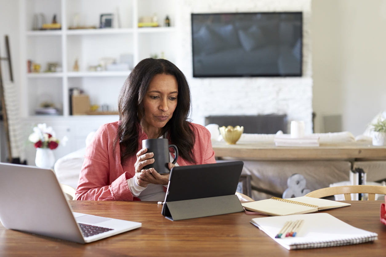 Middle aged woman sitting at a table reading using a tablet computer holding a cup front view Middle aged woman sitting at a table reading using a tablet computer holding a cup front view
