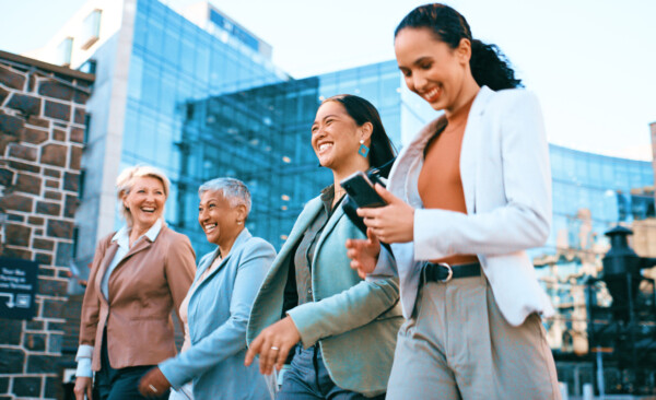 Diverse Group Of Professional Women Walking And Smiling Outdoors In Business District